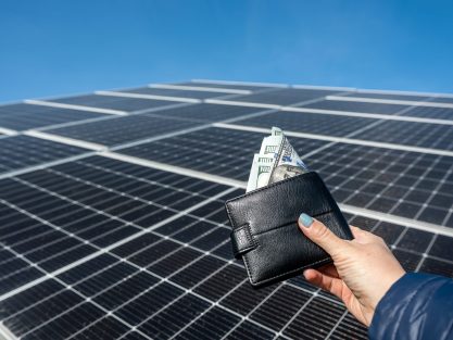 beautiful female hand holds a black wallet with dollar bills, which she holds close to the sun. concept of green electricity. business. purchase of solar panels